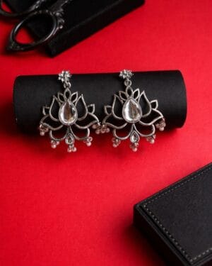 Lotus design oxidised silver drop earrings with teardrop stone and pearl bead detailing on red background