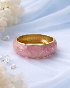 Gold-toned pink resin finish statement bangle placed on white fabric background